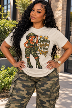 Load image into Gallery viewer, A woman wearing a white graphic t-shirt with a military-themed cartoon design and the text 'Confidence Leads Good ON EVERY Woman' paired with camouflage cargo pants, posing outdoors.