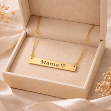 Load image into Gallery viewer, Gold necklace with 'Mama' and heart engraving in a box on a soft beige background