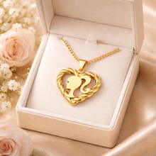 Load image into Gallery viewer, Gold necklace with heart-shaped pendant featuring a Barbie head siloam, displayed in an open jewelry box with flowers in the background.