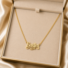 Load image into Gallery viewer, A gold nameplate necklace spelling 'Eagles' with a small eagle motif, displayed inside an open beige jewelry box on a satin fabric background.