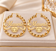 Load image into Gallery viewer, A pair of large gold hoop earrings displayed on a beige jewelry box. Each hoop features the name 'Maunie' in raised script with a small Betty Boop face below it, surrounded by a twisted rope border.