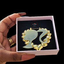 Load image into Gallery viewer, Gold Barbie head earring in a box held by a hand.