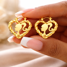 Load image into Gallery viewer, Gold heart-shaped earrings with a heart design with a silhouette of Barbie held by a hand