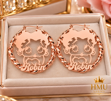 Load image into Gallery viewer, A pair of rose gold hoop earrings with a cutout cartoon character and the name 'Robyn' written along the bottom, presented in a beige jewelry box. The HMU LADIES logo is visible in the bottom right corner.