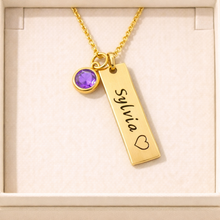 Load image into Gallery viewer, Gold necklace with a name tag and purple gemstone on a beige background