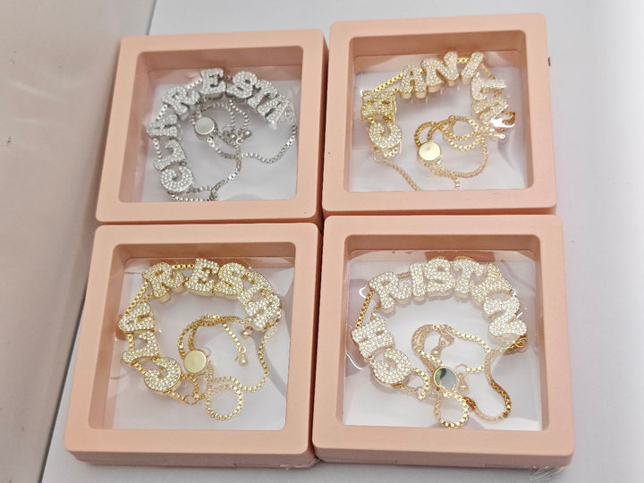 Personalized crystal name bracelets in gold and silver displayed in pink jewelry boxes