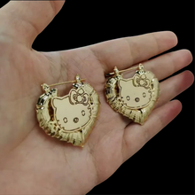 Load image into Gallery viewer, Gold Hello Kitty earrings held in a hand against a black background
