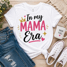 Load image into Gallery viewer, White t-shirt with 'In my MAMA Era' text, paired with jeans, sneakers, and a mug on a wooden surface.
