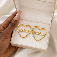 Load image into Gallery viewer, Gold heart-shaped earrings with 'Hello Ladies' text in a white jewelry box held by a hand.
