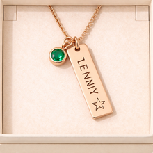 Load image into Gallery viewer, Rose gold necklace with a green gemstone and engraved name tag on a beige background
