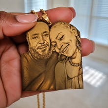 Load image into Gallery viewer, Gold pendant with engraved portraits held by a hand
