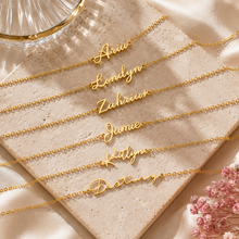 Load image into Gallery viewer, A group of gold name necklace laid out on a display table.
