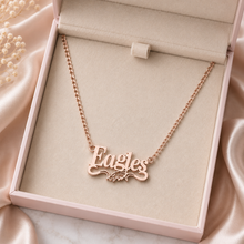 Load image into Gallery viewer, A rose gold nameplate necklace spelling 'Eagles' with a small eagle motif, displayed inside a light pink jewelry box on a beige velvet lining, surrounded by soft pink satin fabric.
