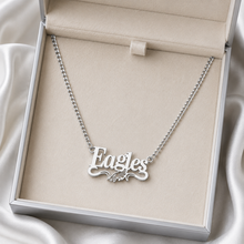 Load image into Gallery viewer, A silver nameplate necklace spelling 'Eagles' with a small eagle motif, displayed inside an open beige jewelry box on a satin fabric background.
