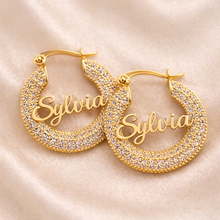 Load image into Gallery viewer, Gold hoop earrings with zirconia stones with thename'Sylvia' engraving on a beige fabric background
